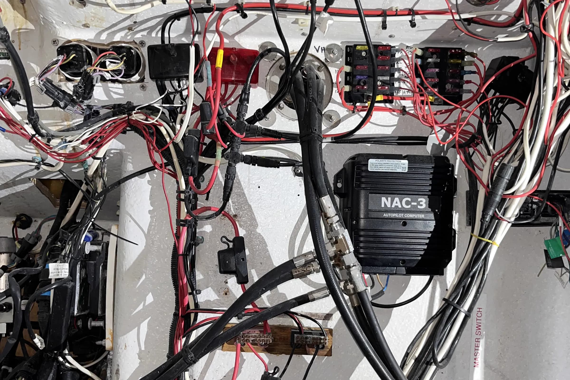 A boat console cavity before rewiring, packed with untied red and white cable crossing a Simrad NAC-3 autopilot computer, with corroded fuse blocks above