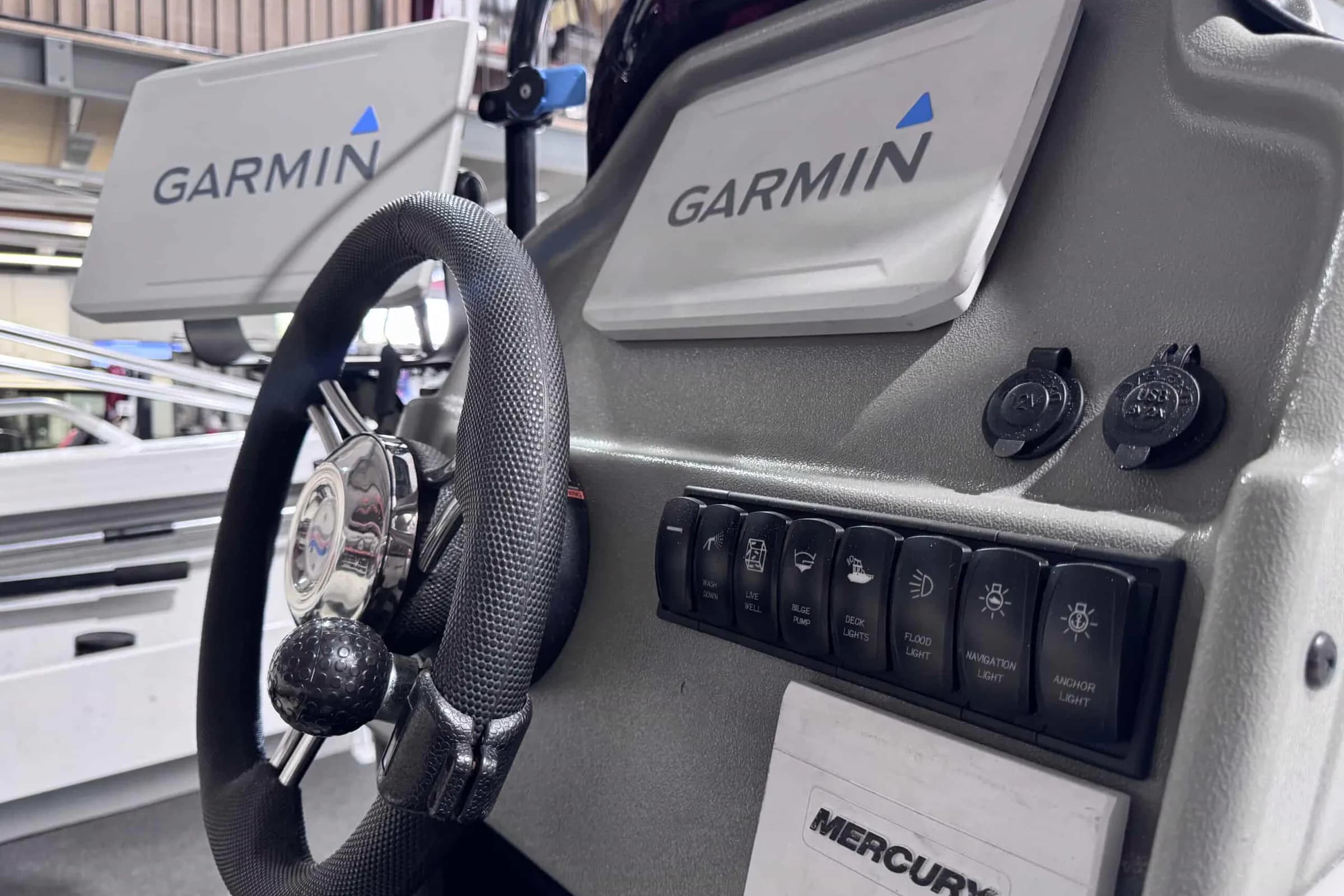 A boat dash with twin Garmin displays, Mercury engine controls and a switch panel labelled wash down, live well, bilge pump, deck lights, flood light, navigation light and anchor light