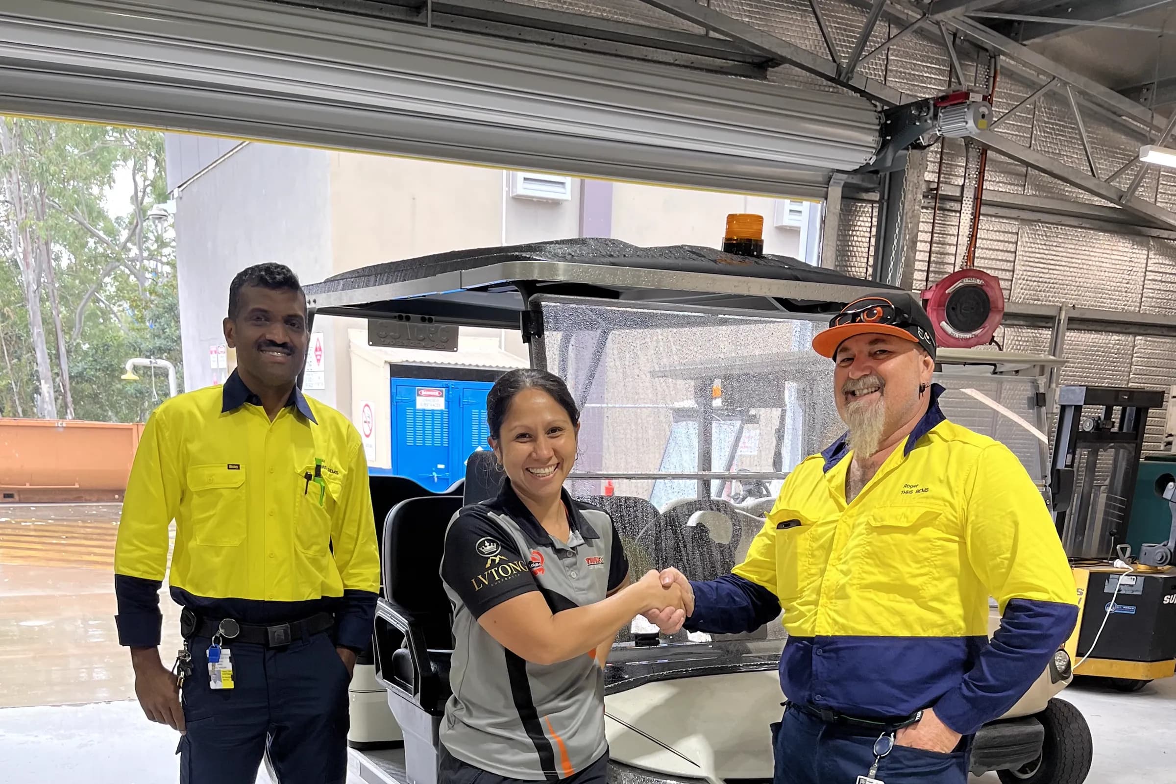 A Townlec staff member shaking hands with a man in hi-vis workwear beside a white utility golf cart at an industrial yard, a second worker looking on