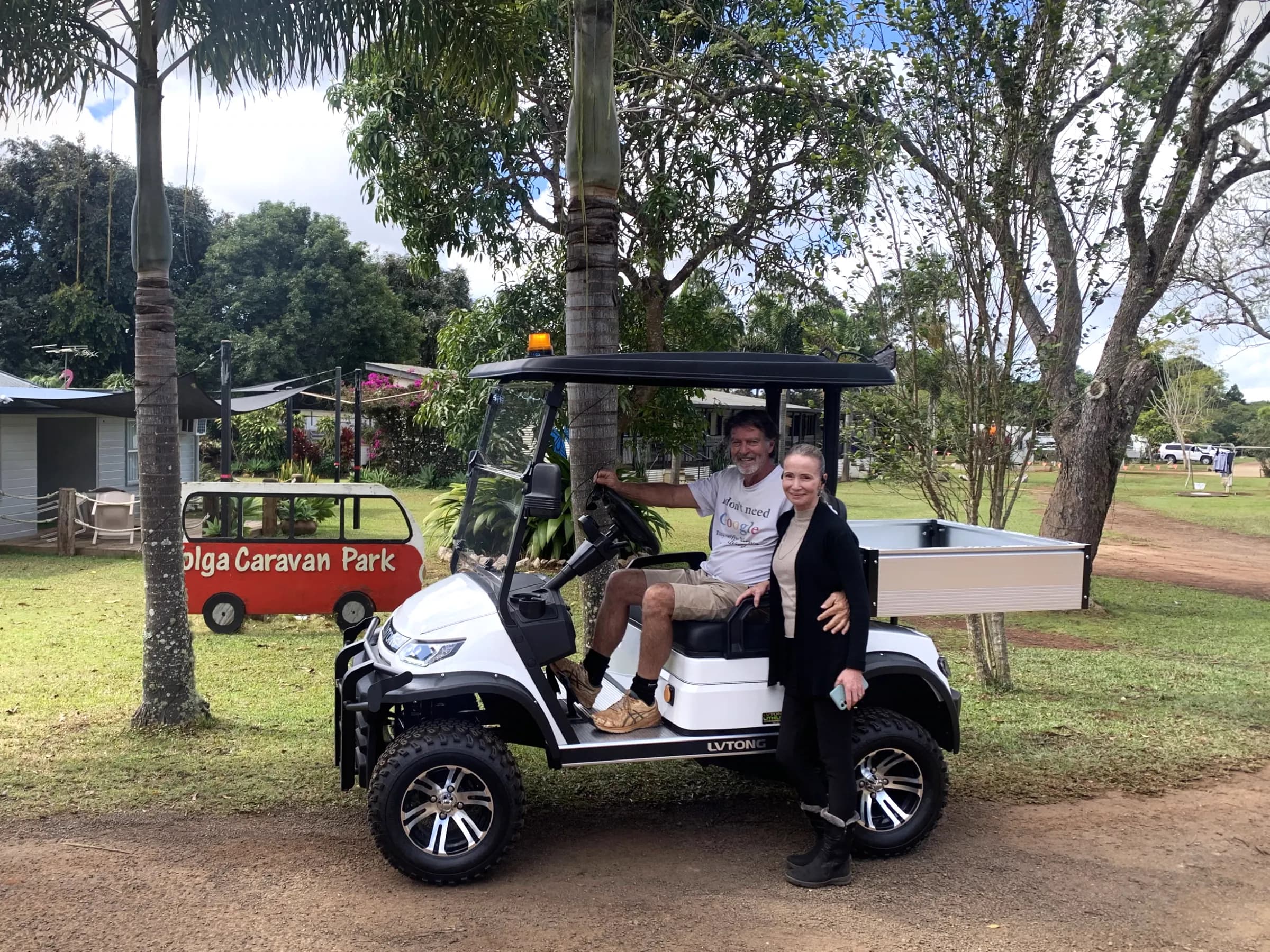 A white LVTong utility cart with a tipping tray and an amber beacon parked at a caravan park