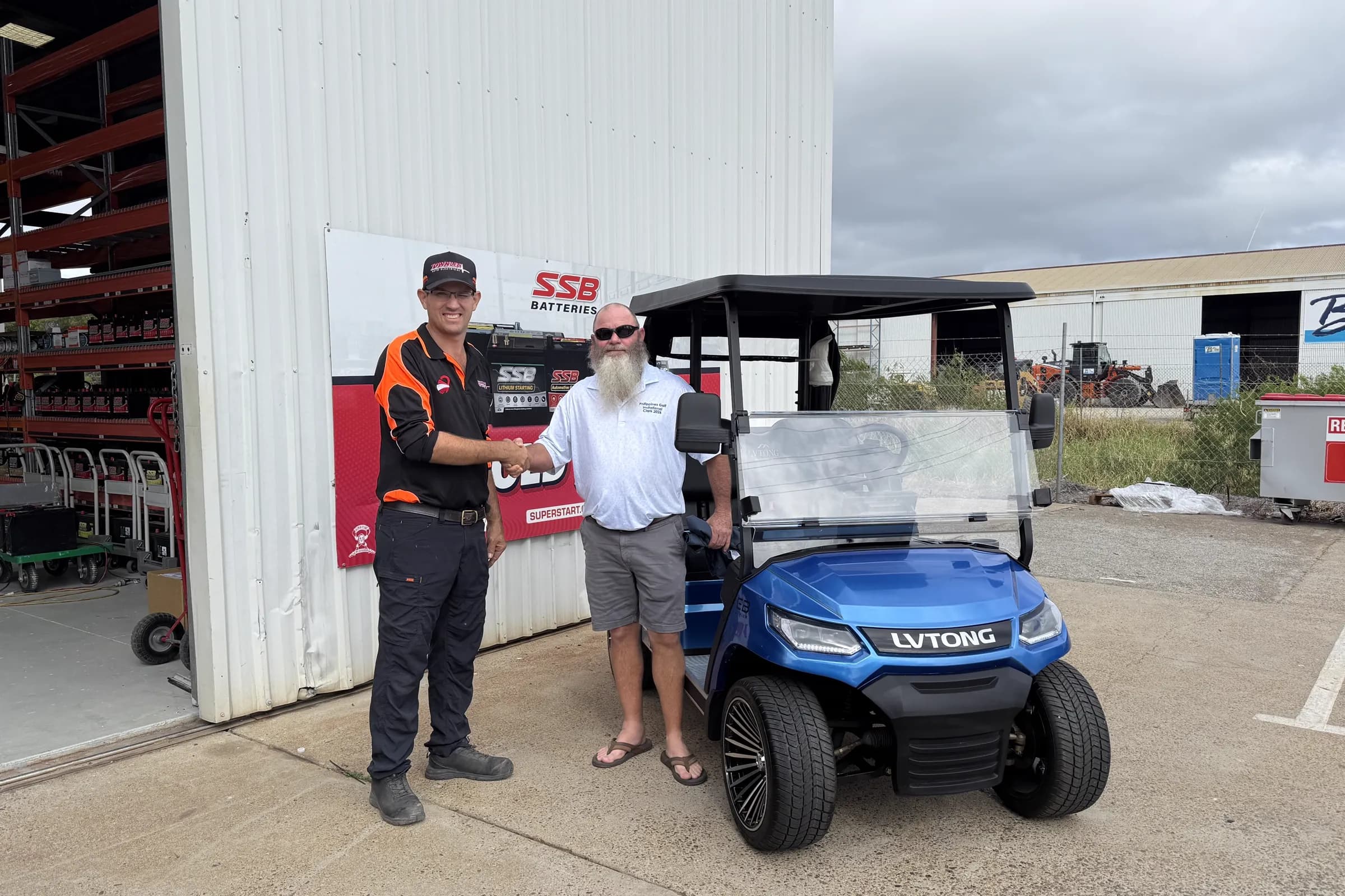 A Townlec staff member shaking hands with a customer beside a blue LVTong golf cart outside the Townsville workshop