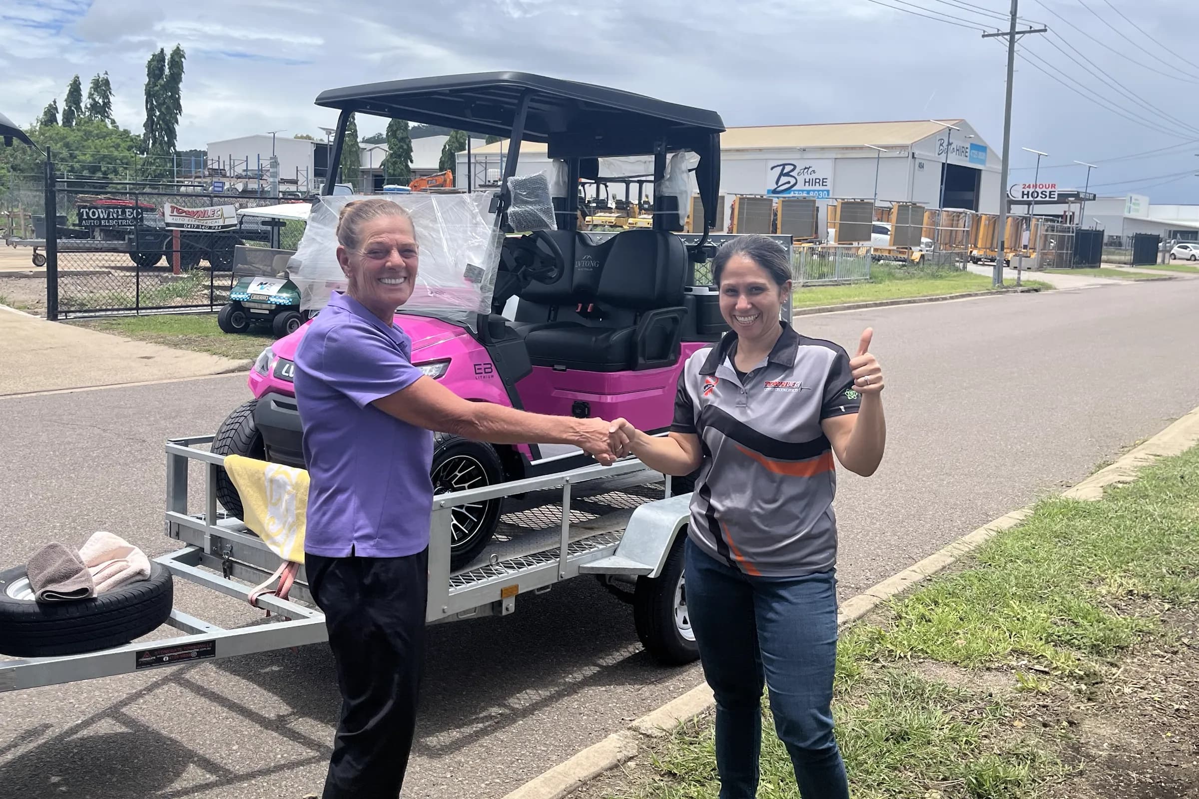 A Townlec staff member shaking hands with a customer beside a pink LVTong golf cart loaded on a trailer