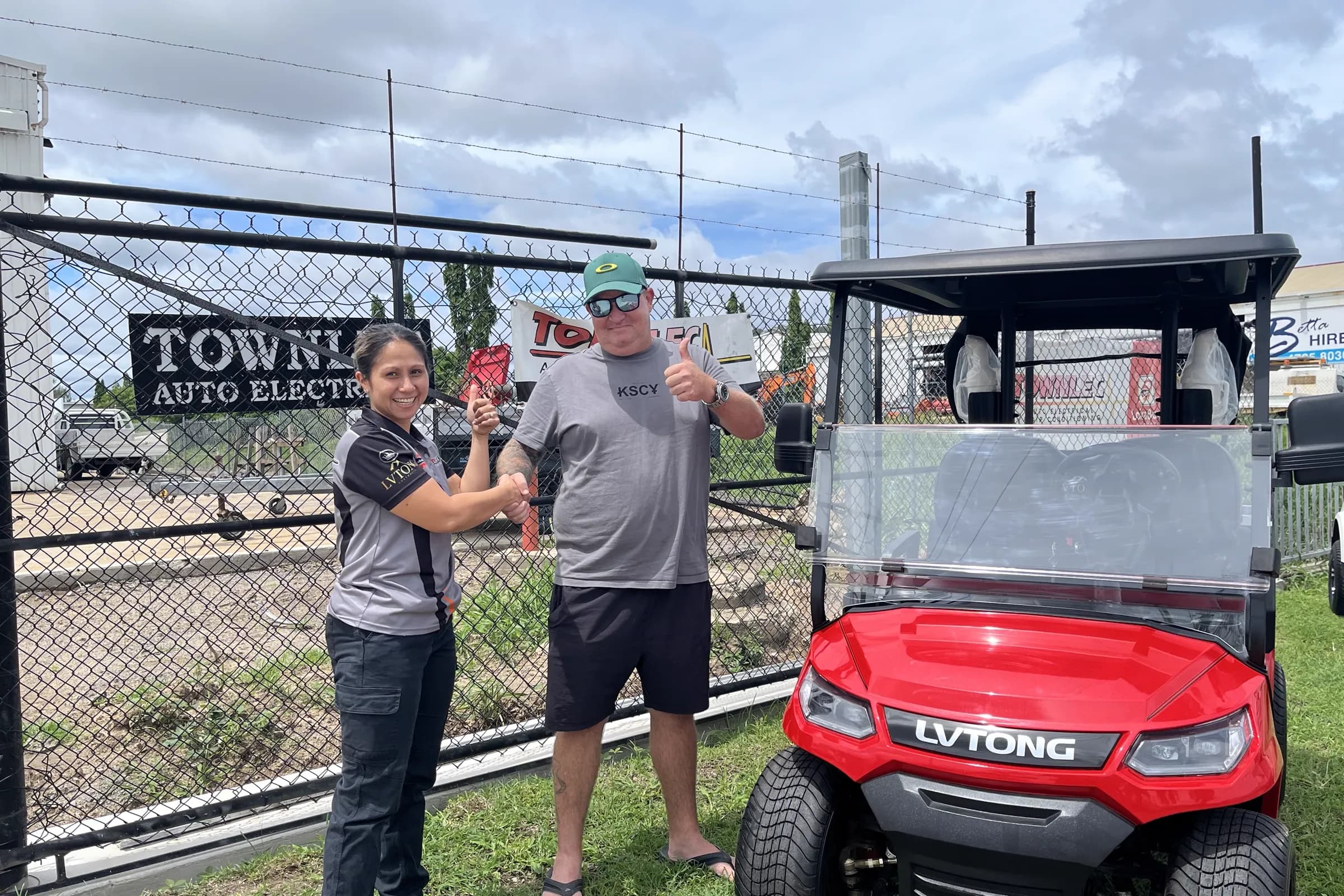 A Townlec staff member shaking hands with a customer beside a red LVTong golf cart on a trailer outside the Townsville shopfront