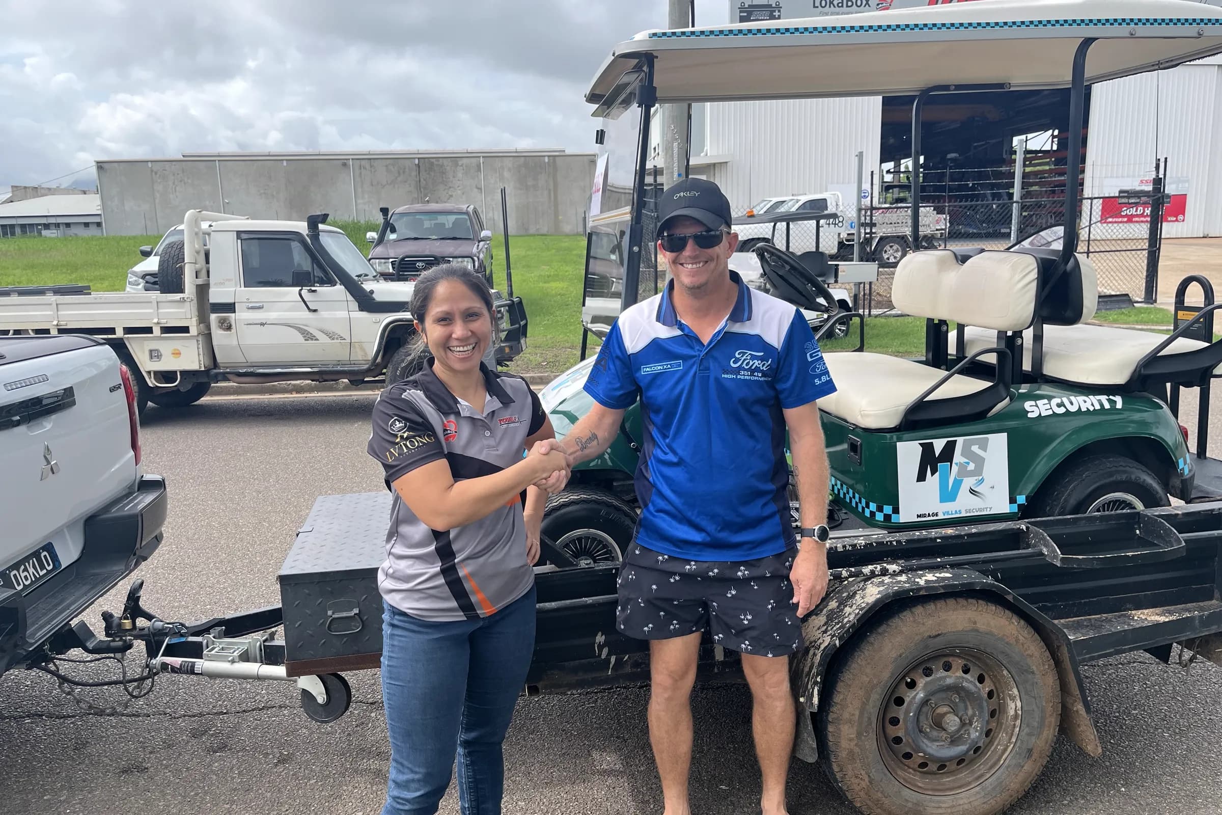A Townlec staff member shaking hands with a customer beside a green second-hand golf cart loaded on a trailer at the Townsville workshop