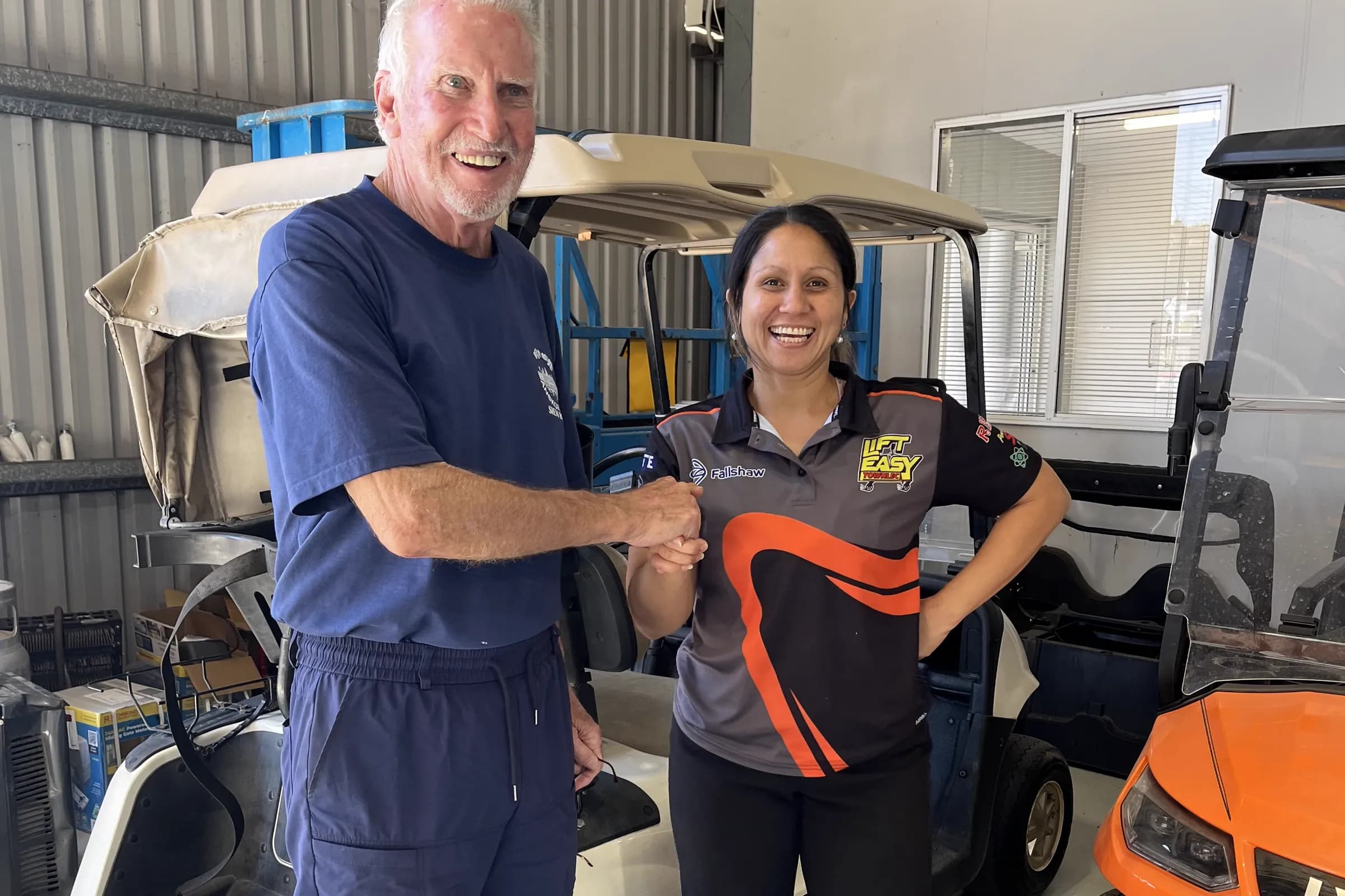 A Townlec staff member shaking hands with a customer beside a used cream golf cart in the workshop