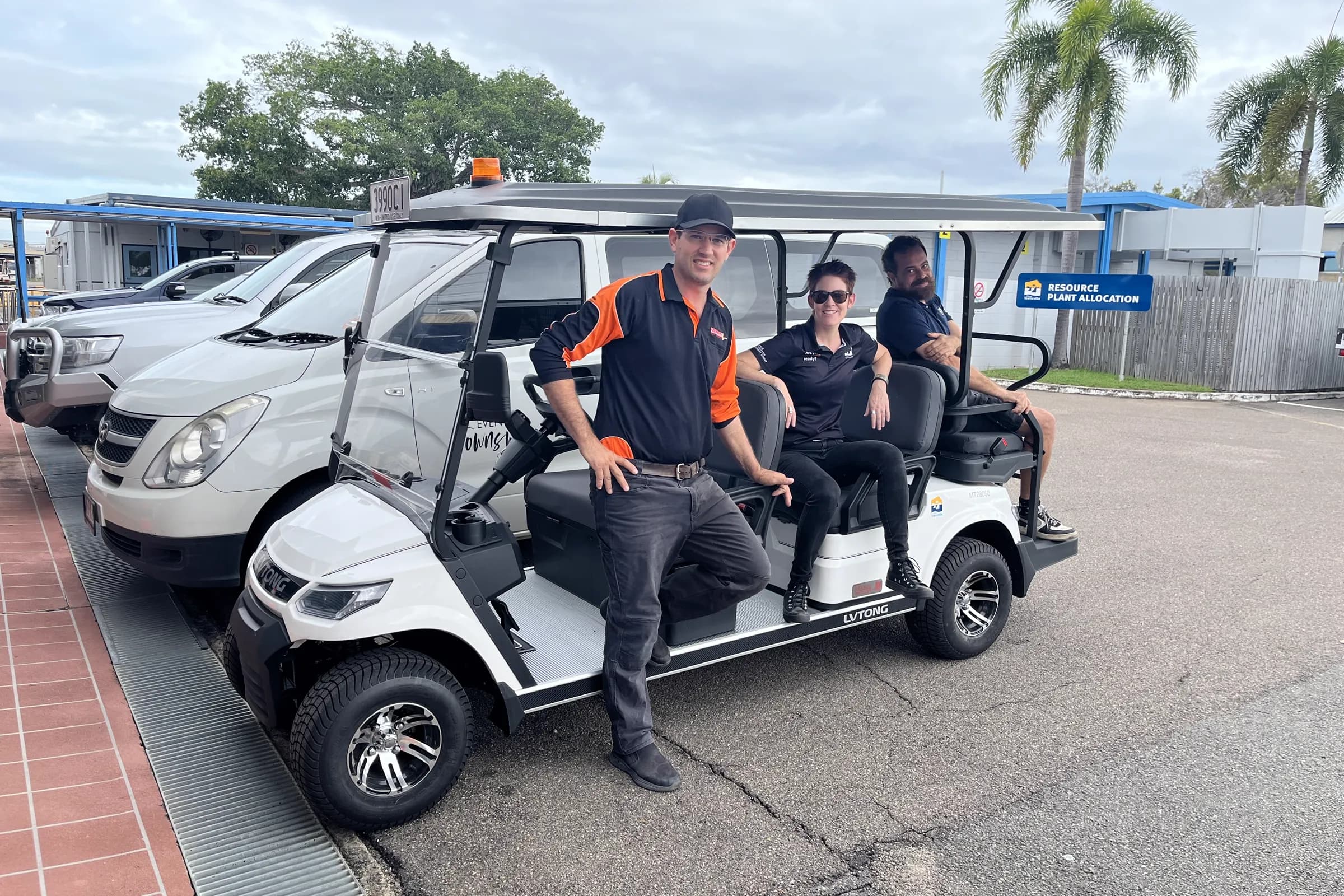 A white LVTong six-seater utility golf cart with a Townlec staff member alongside and two people seated, parked at an industrial depot
