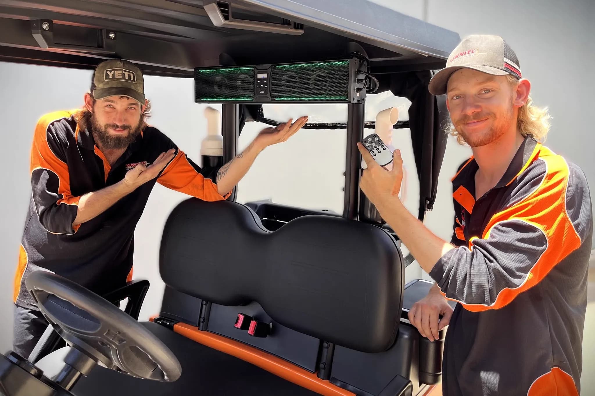 Two Townlec staff either side of a golf cart with a Bluetooth sound bar fitted under the roof, one holding the remote