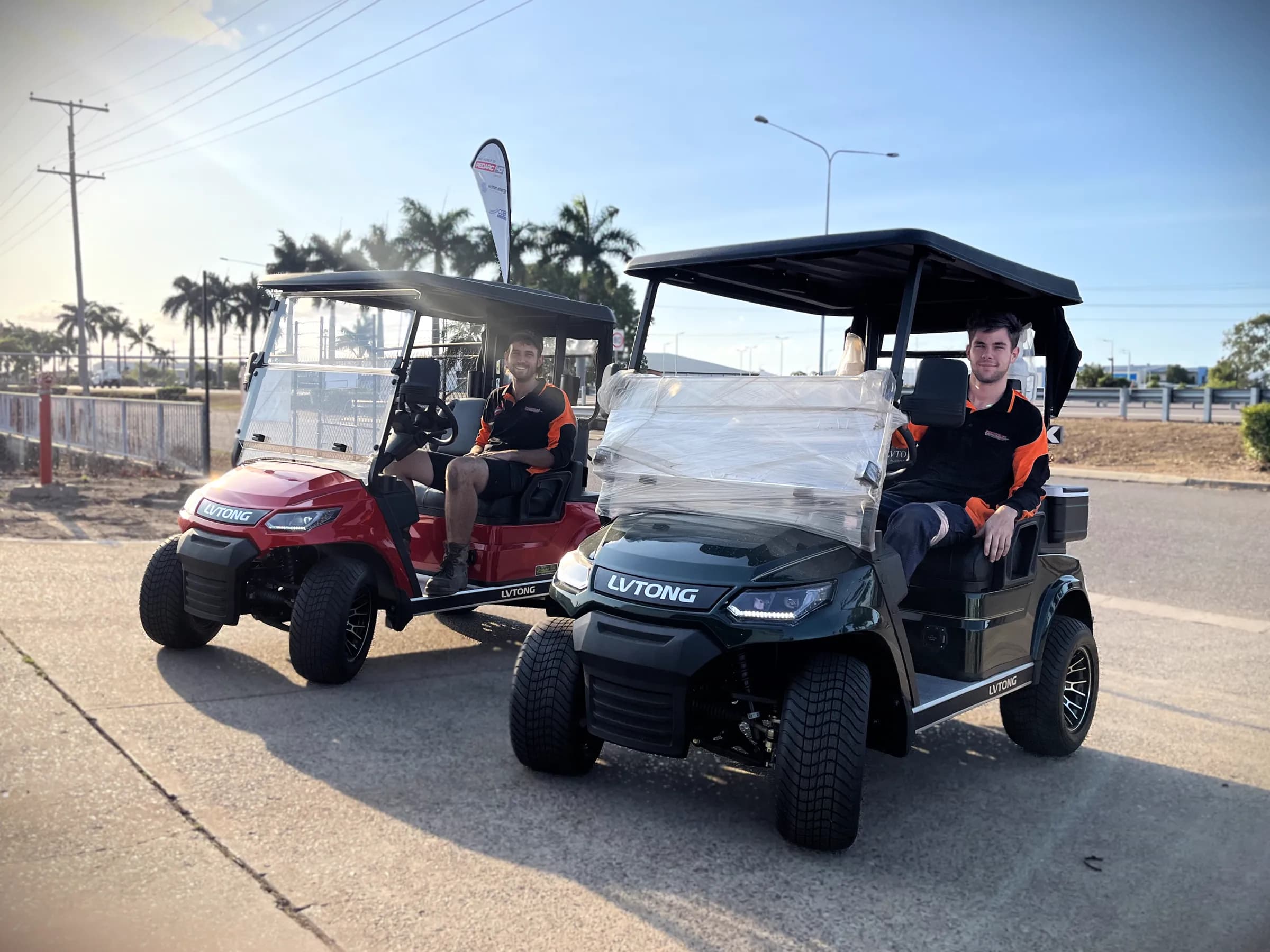 Two new LVTong golf carts, one red and one dark green, outside the Townlec workshop in Townsville with staff sitting in them