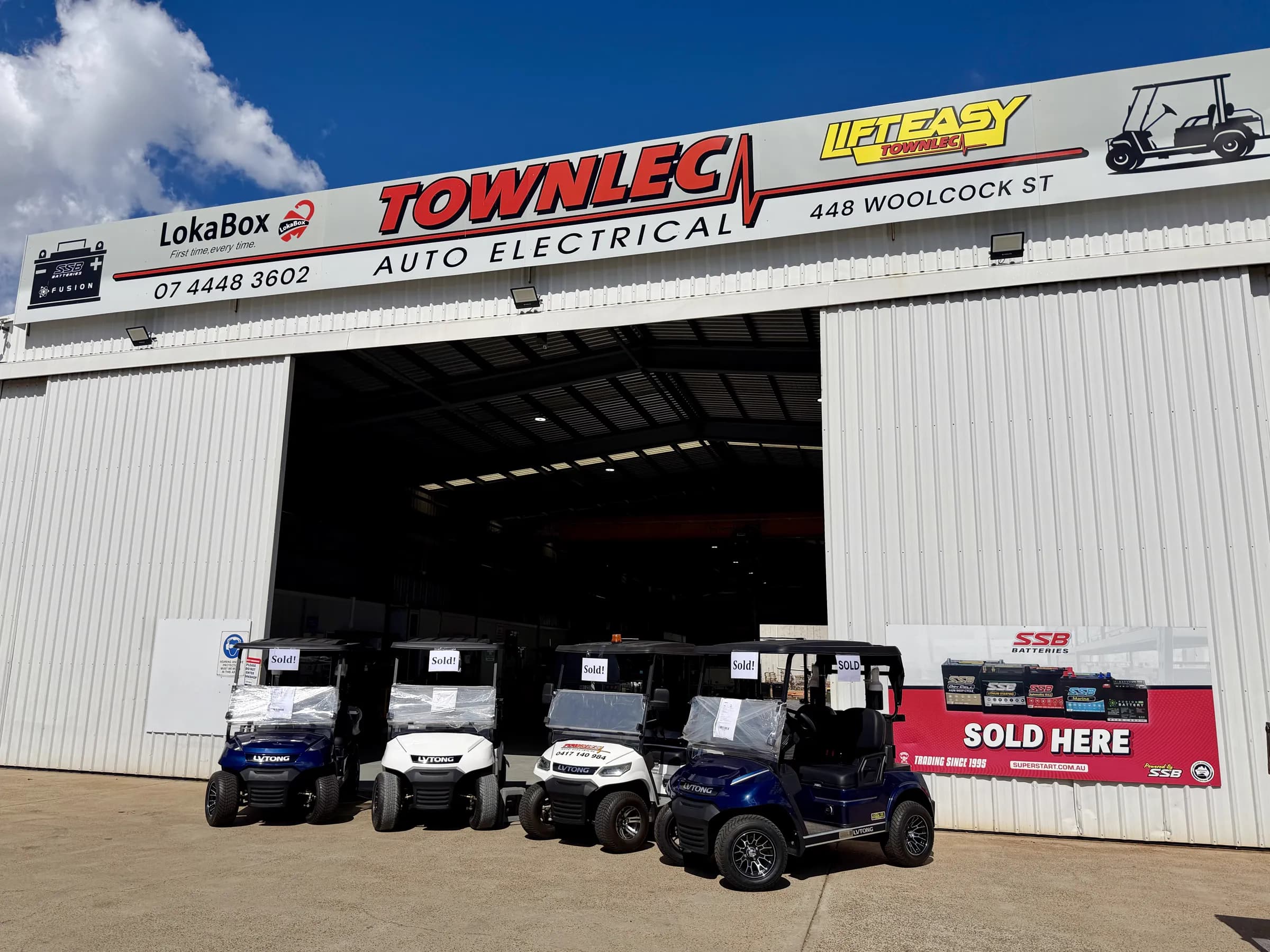 Four new LVTong golf carts lined up outside the Townlec Auto Electrical shopfront on Woolcock Street, each carrying a Sold sign