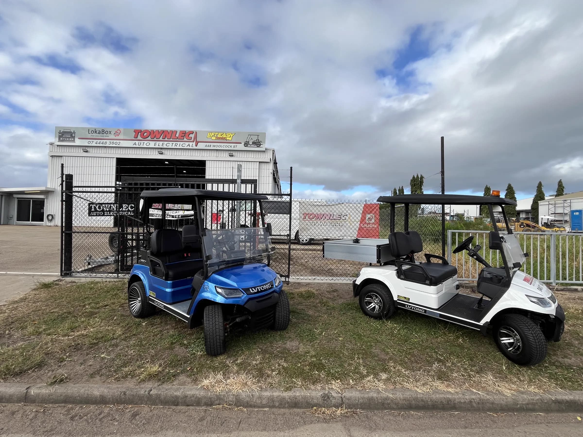 A blue and a white LVTong golf cart parked on the verge in front of the Townlec Auto Electrical building on Woolcock Street, Townsville