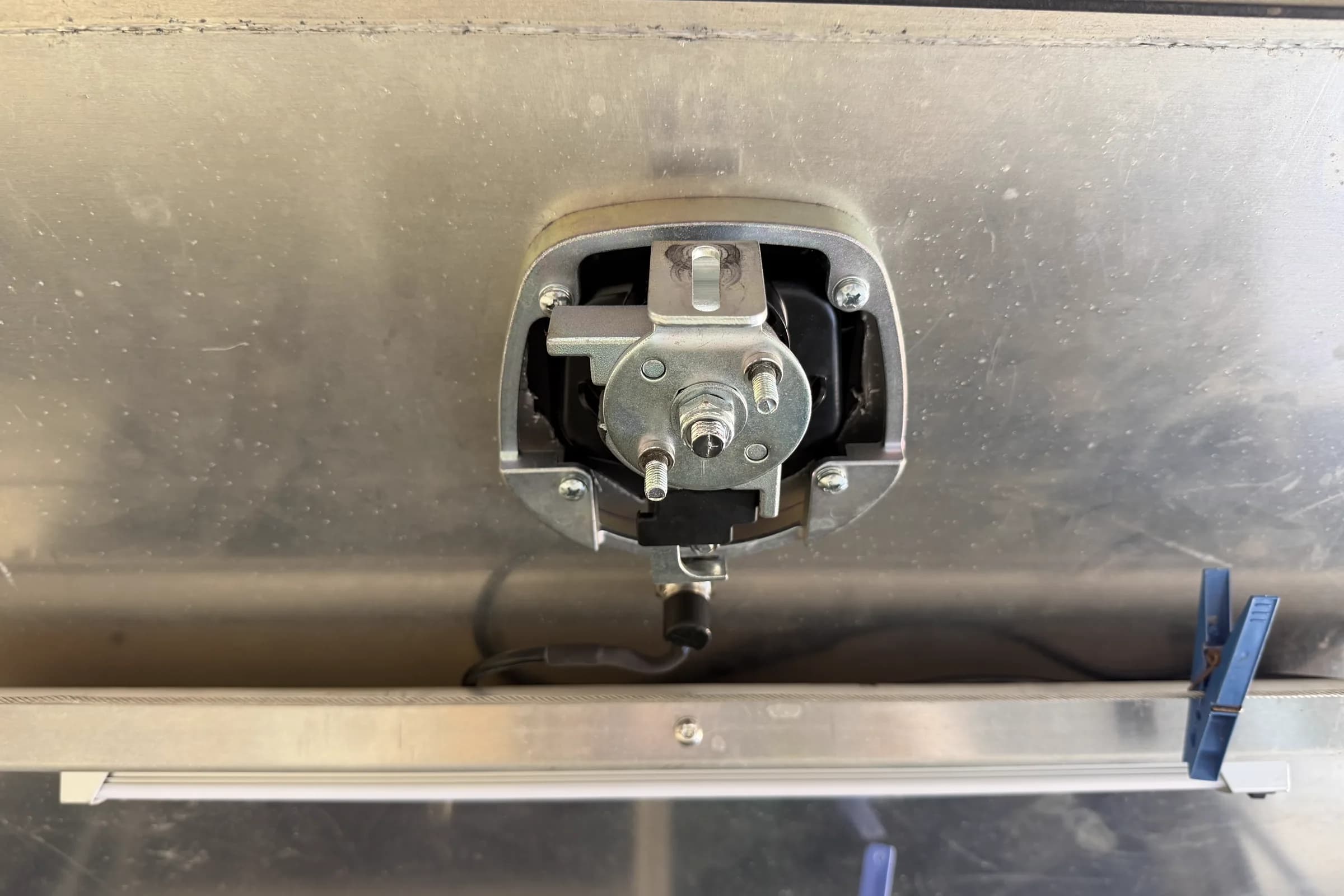 An electric latch actuator mounted behind the T-handle cutout of an aluminium service body, with its wiring run below