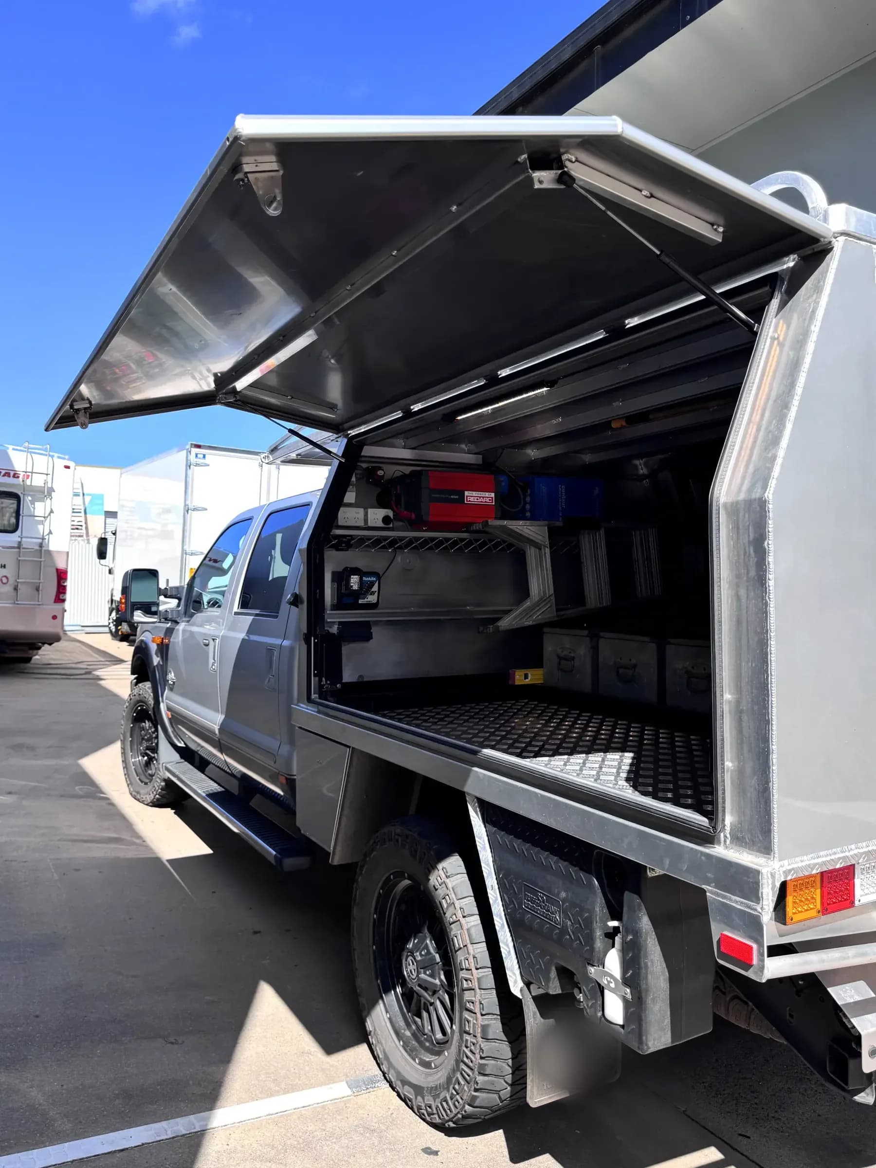 Alloy service body on a Ford F-series with the gullwing door raised, showing shelving, drawers and mounted power equipment