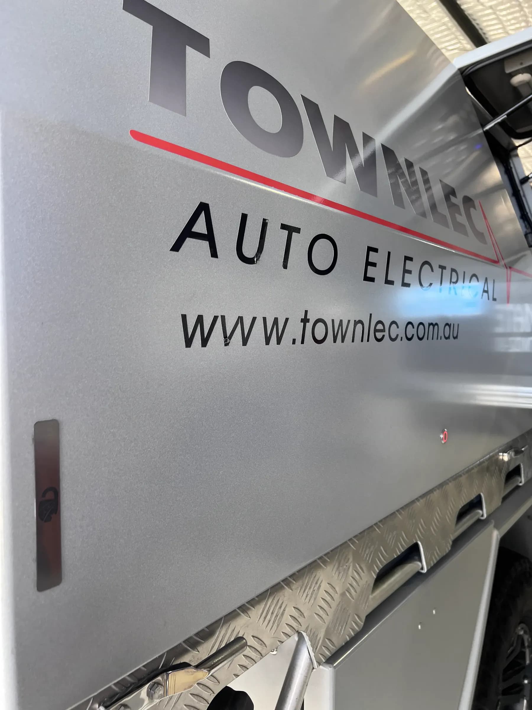 Close-up of a LokaBox press-button release and badge plate on the side of a Townlec-branded alloy canopy