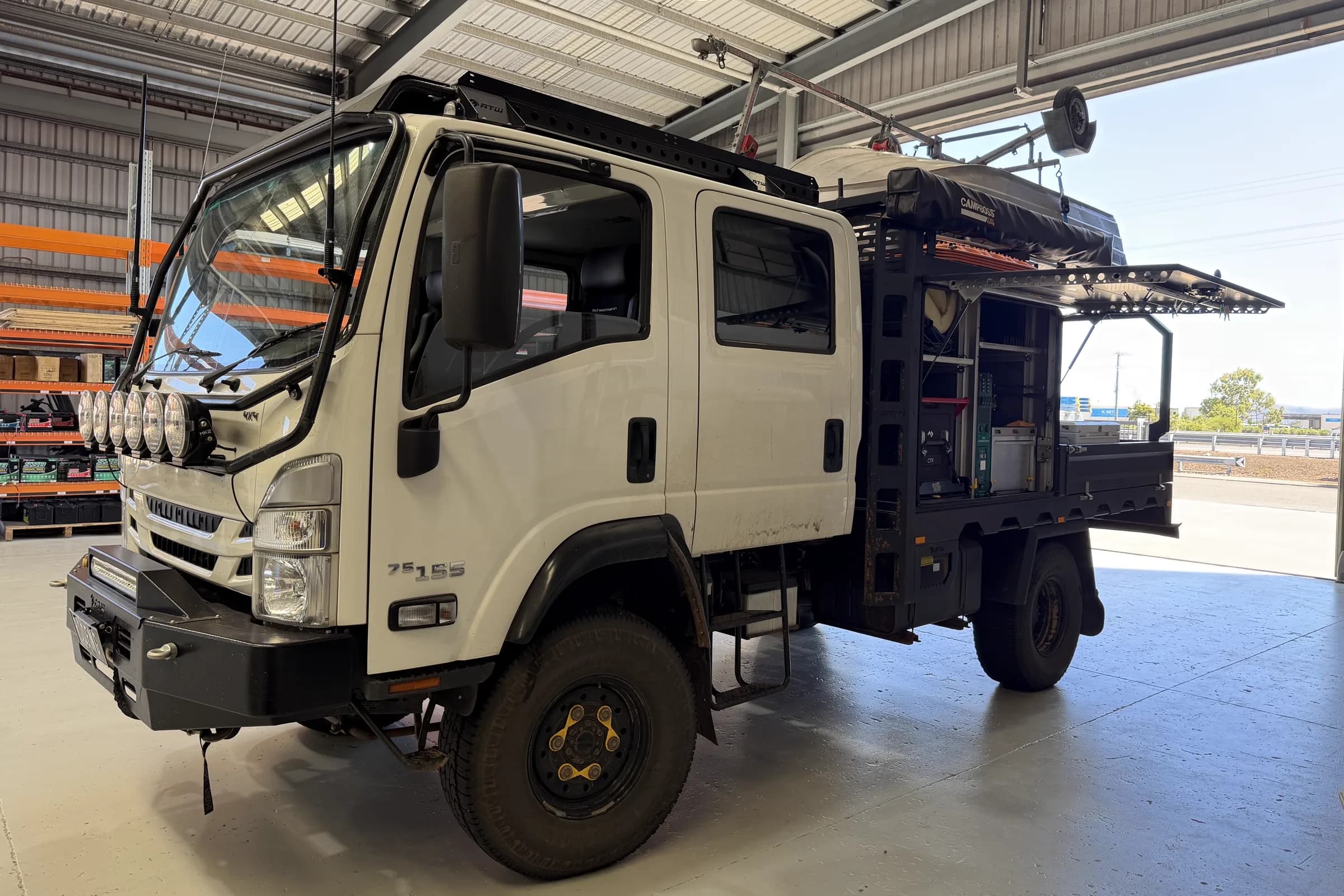 A white Isuzu 75-155 4x4 dual cab with a black canopy and service body in the Townlec workshop, side door open showing the fit-out inside