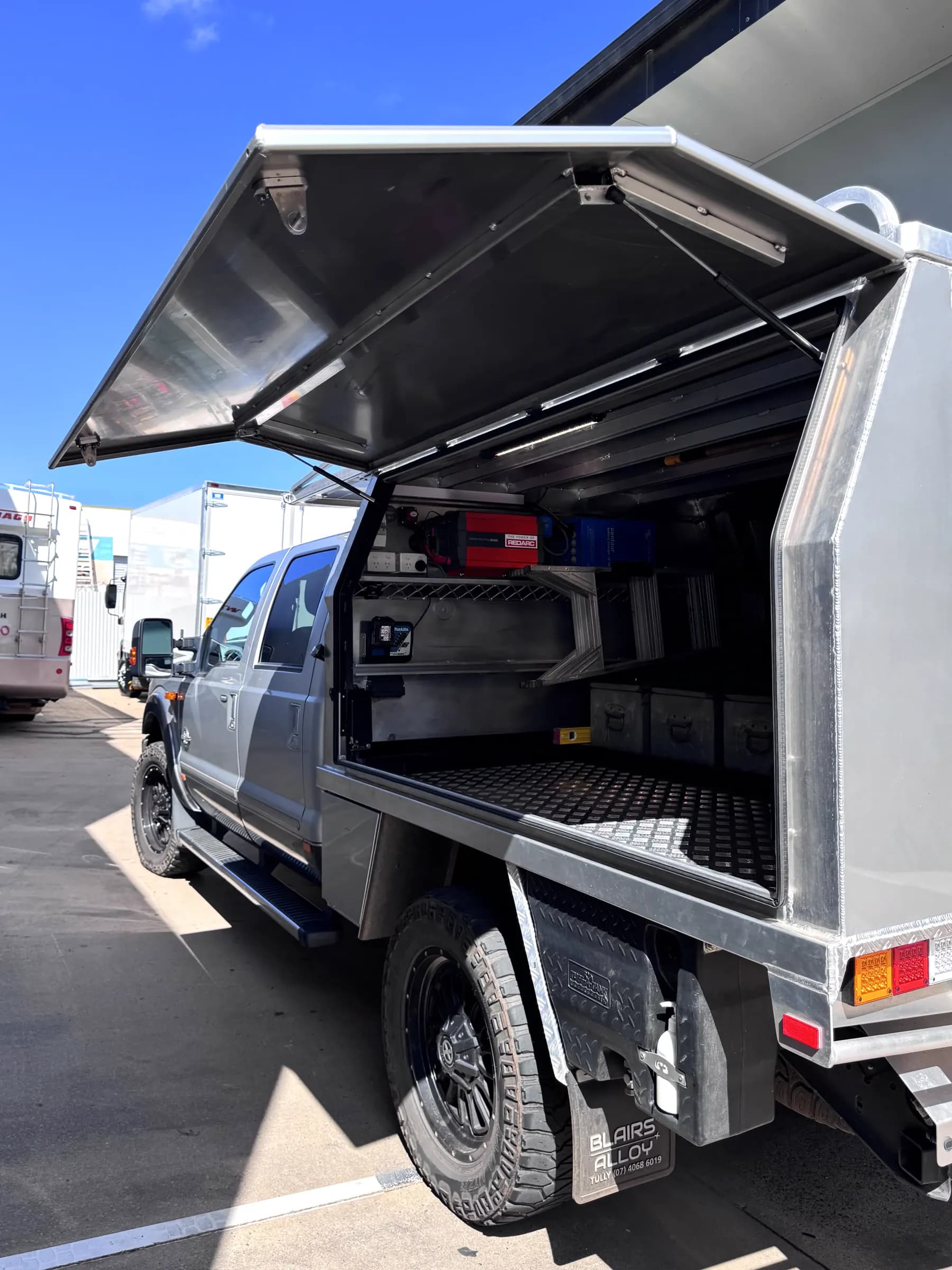 Alloy service body on a Ford F-series with the gullwing door raised, showing shelving, drawers and mounted power equipment
