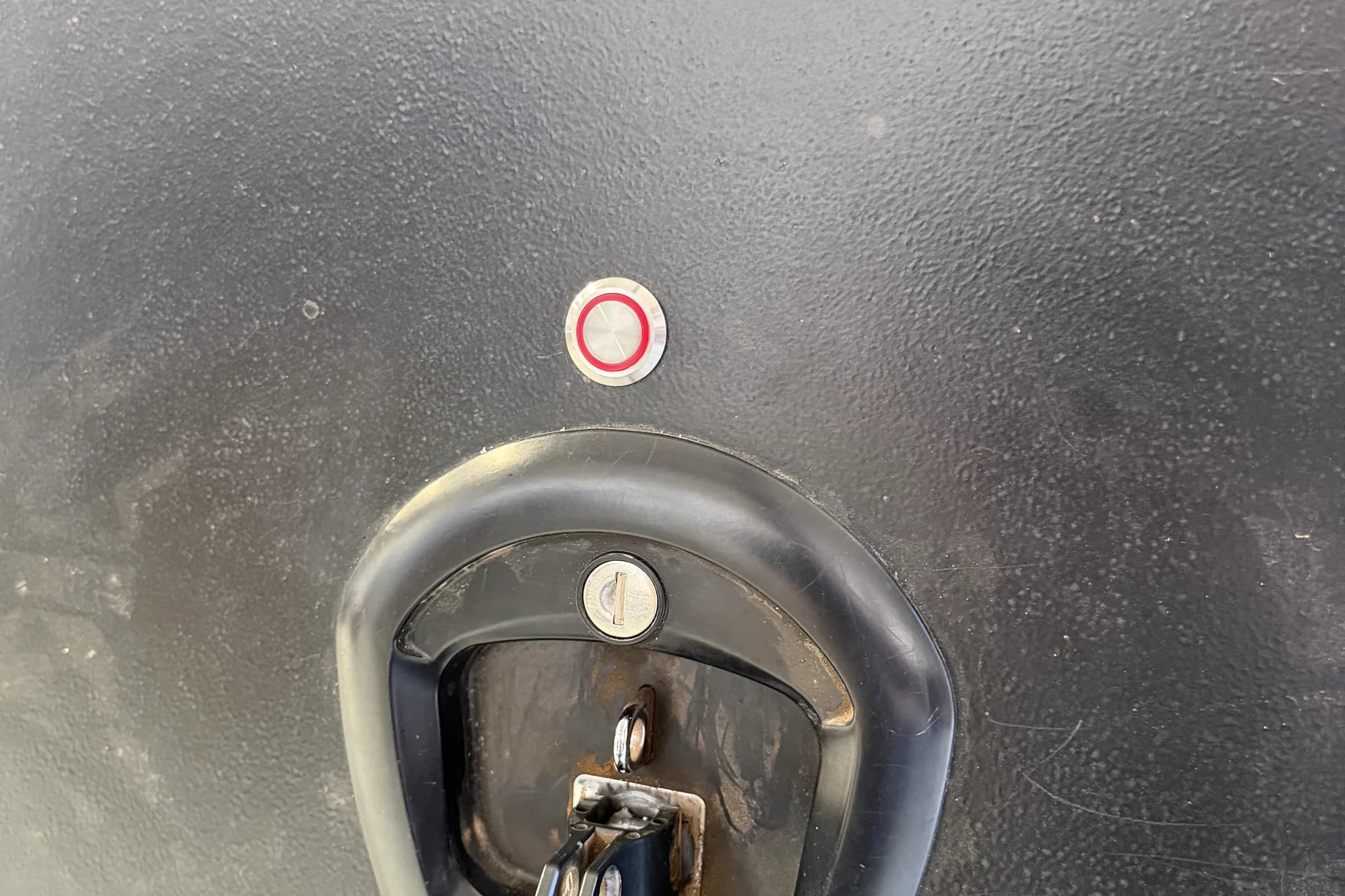 A red-lit LokaBox status light on a black canopy door beside a recessed T-handle and key barrel