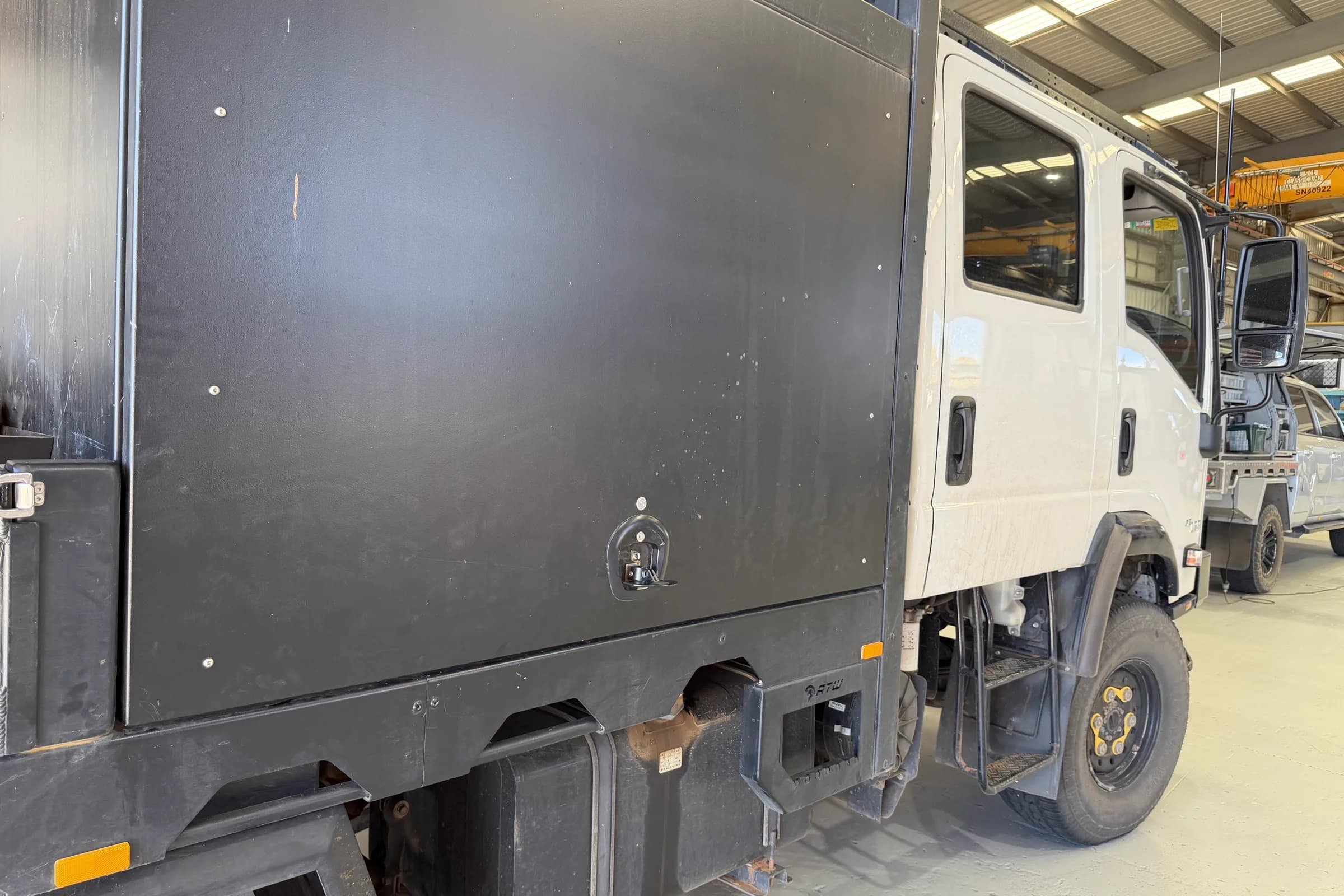 The full side of a black canopy on a white Isuzu truck, with a single recessed T-handle on a large door