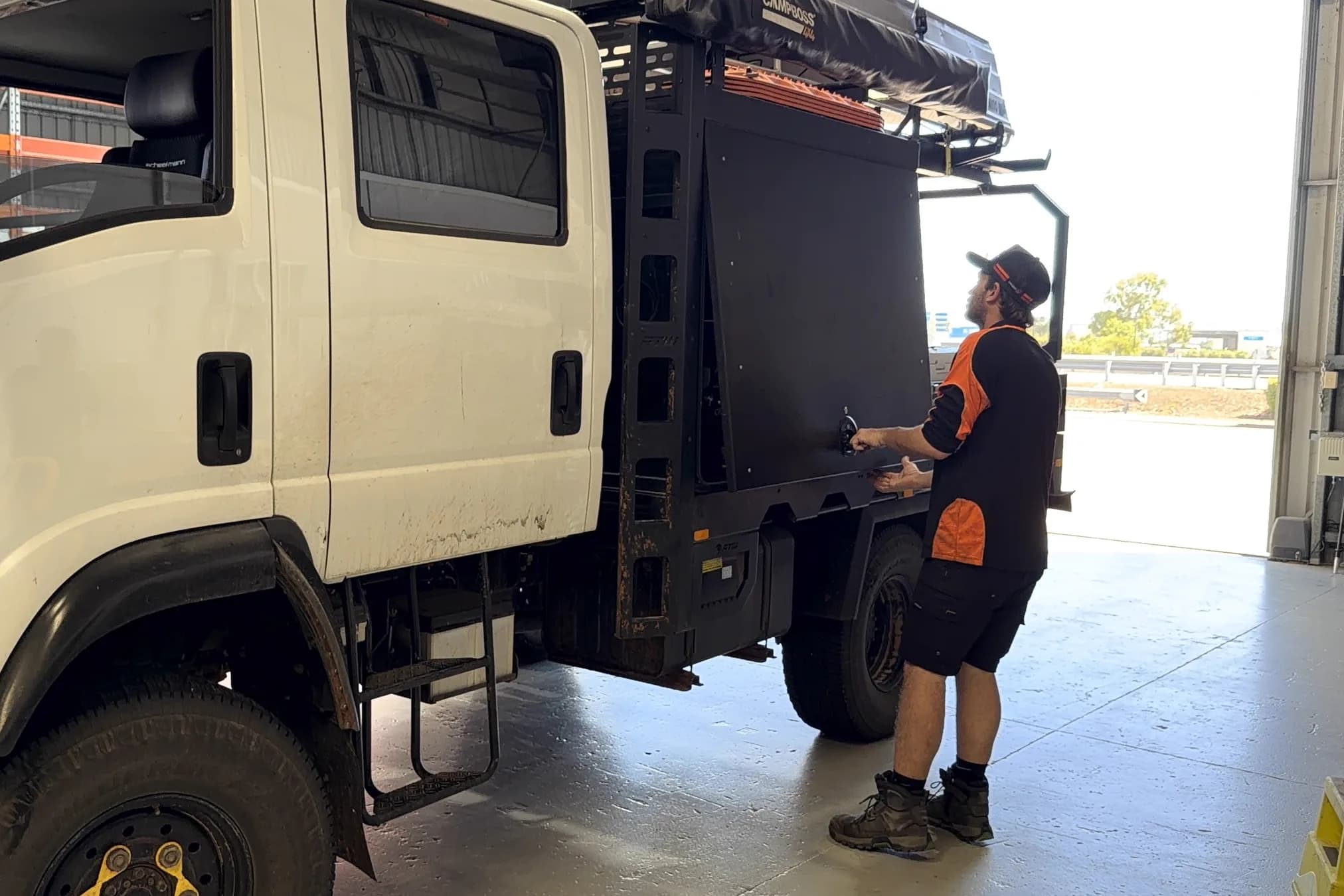 A Townlec technician in hi-vis opening the canopy door of a white Isuzu 4x4 by its T-handle at the Townsville workshop