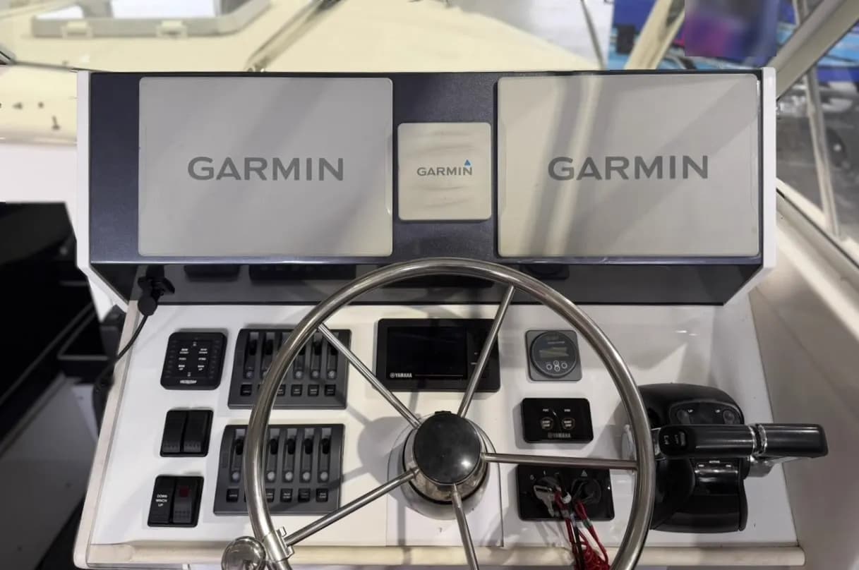 A boat helm with two Garmin displays above a stainless wheel, switch banks either side and Yamaha gauges and binnacle control to starboard